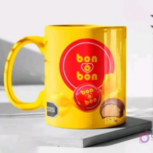 Taza de cerámica color amarillo brillante sublimada con el diseño del bombón Bon o Bon, en un mockup sobre una base gris clara.