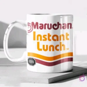 Taza de cerámica color blanco brillante sublimada con el diseño de la sopa instantánea Maruchan Instant Lunch y su etiqueta de advertencia, en un mockup.