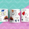 Tazas blancas con diseños de Flork Vol. 3: frases de amor y superación como 'Te llevaste mi tristeza con flores y colores', 'De la mano', 'A tu lado'.